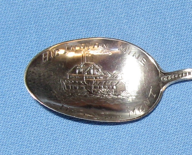 Big Indian Mine Helena MT Bowl Closeup.JPG - SOUVENIR MINING SPOON BIG INDIAN MINE HELENA MONTANA - Sterling demitasse spoon wiith engraved mine buildings in bowl, handle with miner holding pick, crossed hammer and gad inseal at top, marked in bowl BIG INDIAN MINE HELENA MONT. reverse marked Sterling, 3 3/8 in. long [The Big Indian mine is located four miles south of Helena in the Helena Mining District in Jefferson County Montana. The two claims, the Alabama and the Gold Hill were located in 1875. The mine was developed from two open cuts; 200 x 300 ft and 75 x 100 ft. The deepest reached 75 ft. Ore was drawn from the cuts through a glory hole and trammed through an adit to the mill. Initially this was a 10 stamp mill, which was reported to have produced $110,000 from $5 per ton gold ore. This mill was replaced by an electric 60-stamp mill in 1902. In 1904 the Big Indian mine was the biggest producer in Jefferson County. Between 1902 and 1904 the mine produced 14,808 tons of ore which yielded 4,456 ounces of gold. In total the mine made $60,000 from ore valued at $5 per ton. The mine apparently shut down shortly after 1904.]